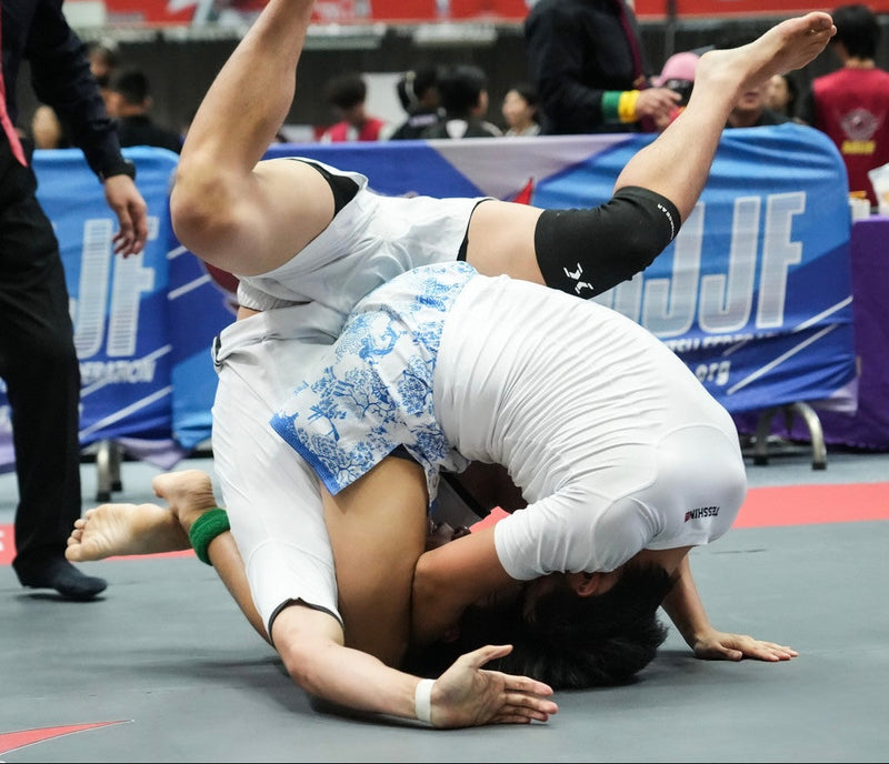 Tesshin athlete sweeps opponent in competition, wearing Porcelain Fightshorts and Marble White Rashguard